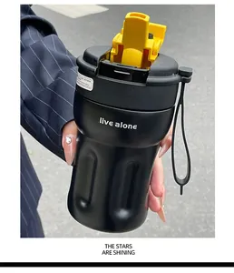 Detail view of a black minimalist coffee cup with a yellow lid and carrying strap