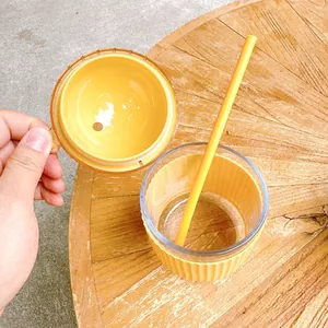 Detailed view of cute yellow glass cup with matching straw and lid on wooden table.