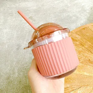 Macro shot of a pink egg-shaped glass cup with ribbed silicone sleeve and straw