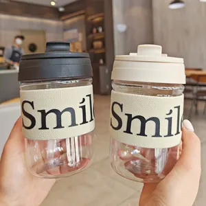 Nahaufnahme von zwei tragbaren Plastik-Kaffeetassen mit Smile-Isolierhüllen im Café-Ambiente