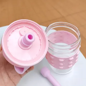 Close-up detail of a pink straw glass water bottle with a heart pattern silicone sleeve
