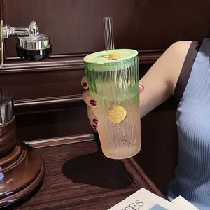 Close-up of gradient green and peach textured glass cup with straw on wooden table