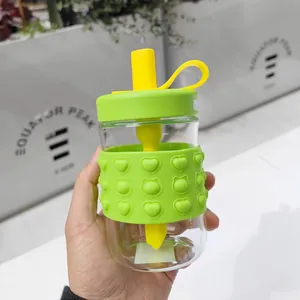 Handheld glass water bottle with lime green heart-patterned silicone sleeve and straw