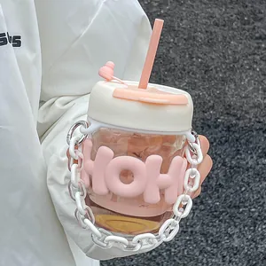 Close-up of a cute pink glass straw cup with a white decorative chain handle held in hand.