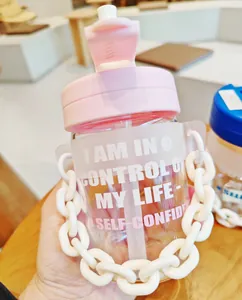 Vue détaillée d'un gobelet portable en verre avec paille, chaîne tendance et texte motivant.