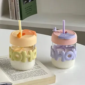 Two cute aesthetic glass straw cups with pastel silicone HOHO sleeves and lids on a book