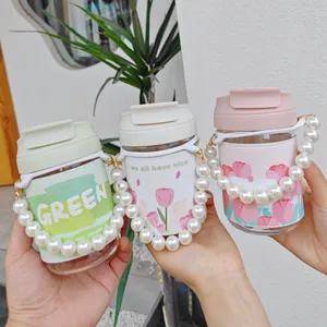 Close-up view of three portable glass water bottles with tulip sleeves and pearl-beaded handles.