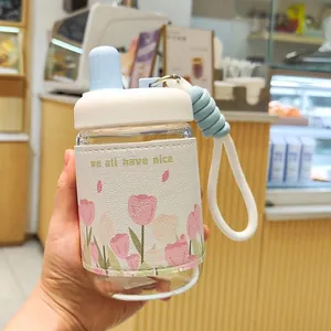 Gros plan d'une bouteille d'eau en verre avec housse isolante aux motifs de tulipes roses