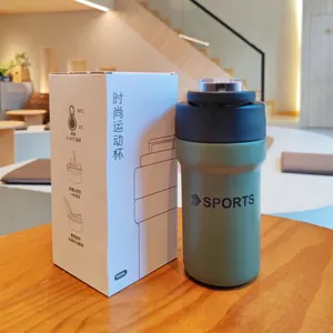 Green insulated sports tumbler with dual-drink lid next to its packaging box on a table