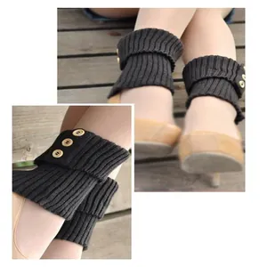 Detail view of black knit leg warmers with three decorative buttons on a wooden floor.