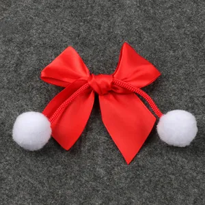 Detalle de lazo de satén rojo de Navidad con pompones blancos para decoración DIY.