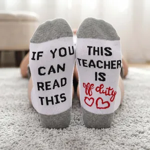 Detailed macro shot of white cotton socks featuring a fun 'Teacher Off Duty' message on the soles.