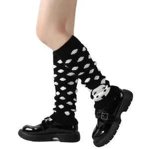 Detail van zwart-witte gebreide beenwarmers met stippen gecombineerd met zwarte schoenen