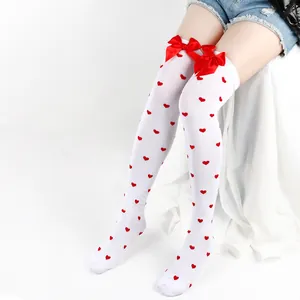 Close-up detail of white over-the-knee socks with red heart patterns and satin bows