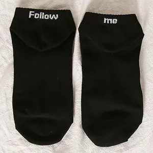 Detail of black low-cut socks with white Follow Me text embroidery on the heels