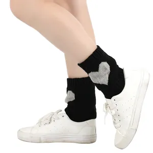 Detailweergave van zwarte gebreide beenwarmers met zilveren hart over witte sneakers