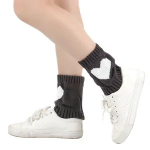 Detailweergave van grijze gebreide beenwarmers met wit hartpatroon over witte sneakers