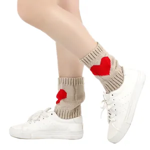 Detailopname van beige gebreide beenwarmers met rood hartpatroon en witte sneakers.