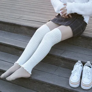 Close-up of white knitted over-knee leg warmers with ruffle edge detail on wooden stairs