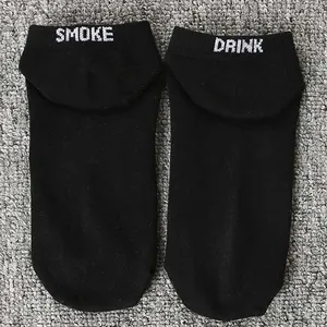 Close-up of black funny socks featuring white embroidered SMOKE and DRINK text on top.