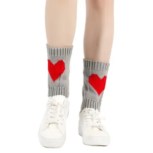 Deze grijze gebreide beenwarmers hebben een rood hartjespatroon en witte sneakers.