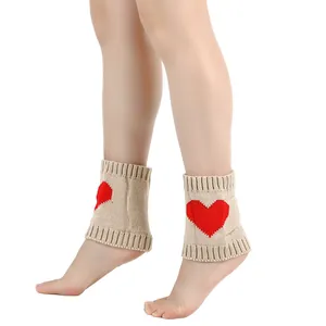 Detailweergave van beige gebreide beenwarmers met een rood hartpatroon en geribbelde rand.