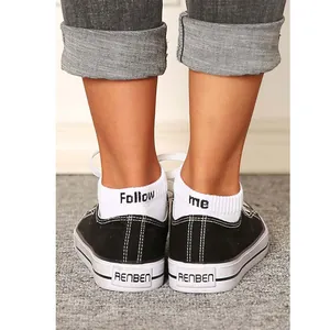 Close-up detail of white cotton ankle socks featuring 'Follow me' embroidery on the heel