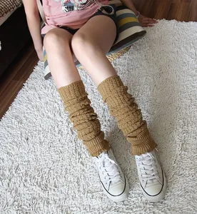 Close-up detail of cozy camel knitted leg warmers styled with white sneakers on a soft white rug.