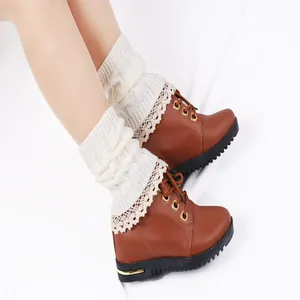 Close-up of white knitted leg warmers with delicate lace trim over stylish brown boots.