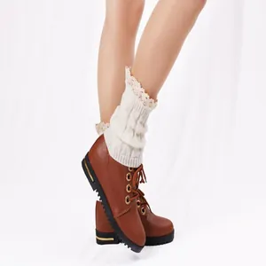 Detail shot of cream knitted leg warmers with elegant lace trim worn over brown boots