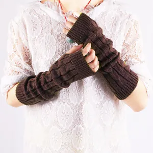Macro view of brown cable-knit fingerless arm warmers worn over a white lace top.