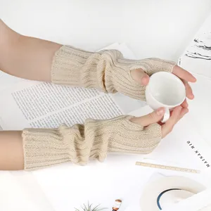 Cozy beige knitted fingerless arm warmers held while gripping a white ceramic cup.