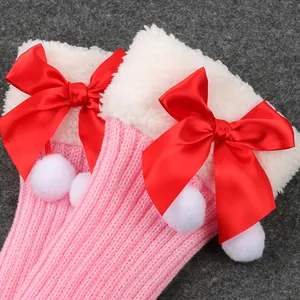 Close-up of pink knitted leg warmers with white fur trim, red bows and pom-poms.
