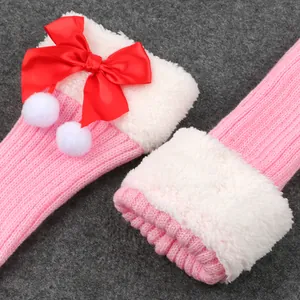 Close-up of pink knitted leg warmers featuring red bows and plush white fur cuffs.