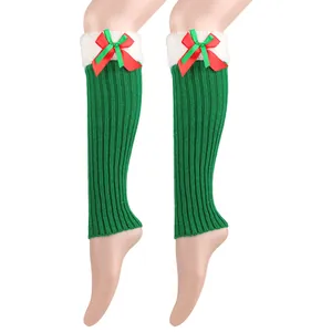 Close-up of green knitted Christmas leg warmers with white plush trim and red bow detail.