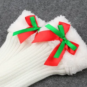Detail shot of white knitted Christmas leg warmers with plush trim and festive bows