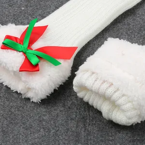 Close-up detail of white plush knitted Christmas leg warmers with red and green bow