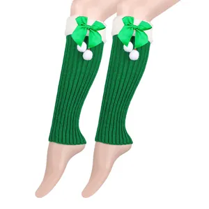 Detailed view of green knitted Christmas leg warmers with bows and white pom-poms