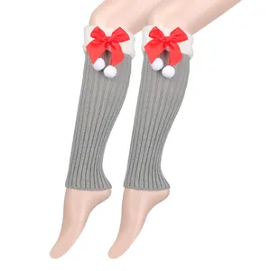 Detailed view of gray knitted leg warmers with festive red bows and white pompoms