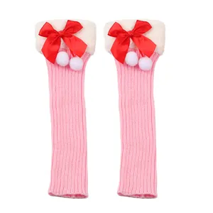 Detailed view of pink knitted leg warmers featuring red bows and white faux fur cuffs.