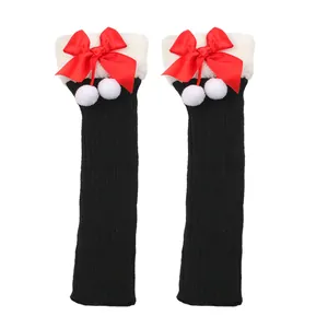 Black knitted leg warmers featuring festive red satin bows and white plush pom-pom details