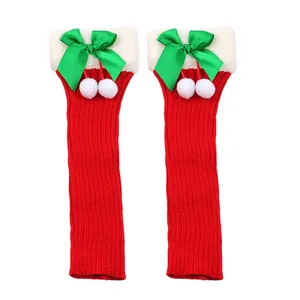 Close-up of festive red Christmas knit leg warmers with green bows and white pom-poms