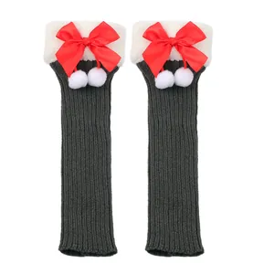 Detailed view of grey knitted leg warmers featuring red satin bows and white pom-poms