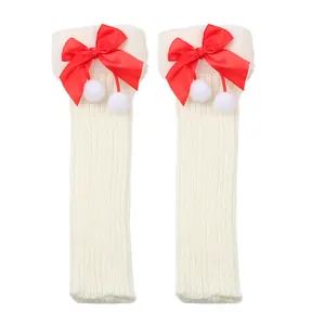 Detailed texture of white knitted leg warmers with red satin bows and white pompoms