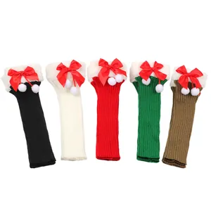 Close-up detail of festive Christmas knitted leg warmers with red bows and white pom-poms