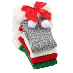Festive knitted Christmas leg warmers featuring red ribbon bows and soft white pom-poms