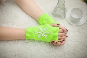 Close-up view of lime green knitted fingerless gloves with white snowflake embroidery