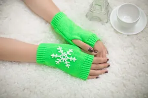 Close-up of bright green knitted fingerless gloves featuring white snowflake applique.