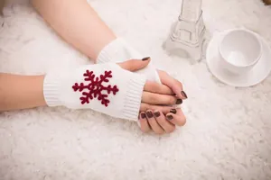 Detailed close-up of white knitted fingerless gloves featuring red snowflake embroidery