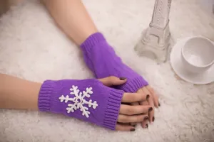 Close-up detail of purple knitted fingerless gloves featuring a decorative white snowflake